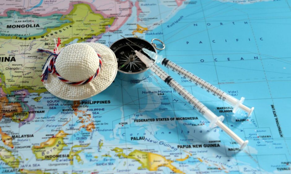 A compass with two disposable syringes and travel cap on world map