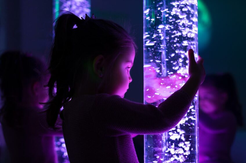 A child touching a cylinder containing bubbles lit by lights