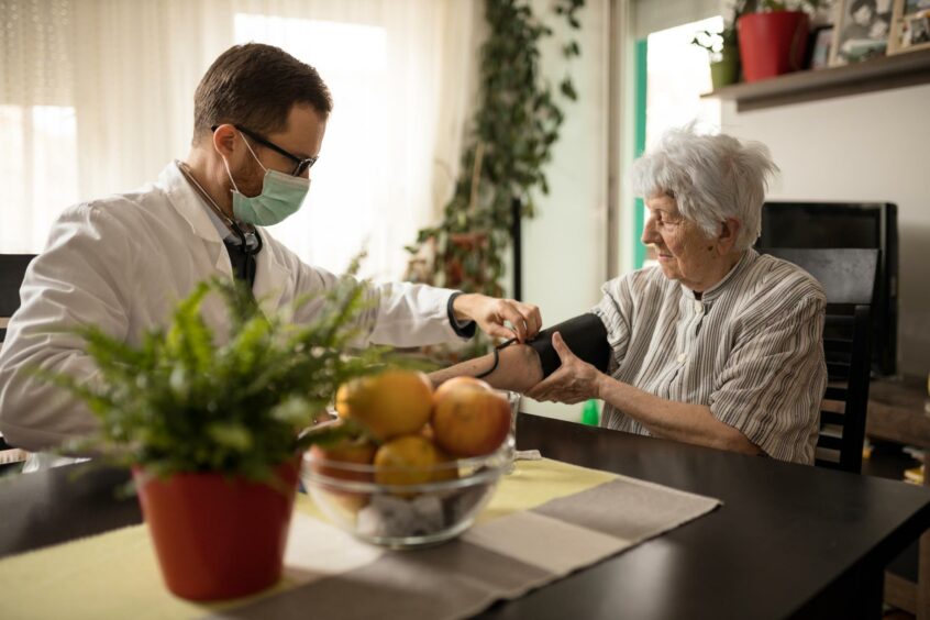 Doctor taking pensioner's blood pressure.