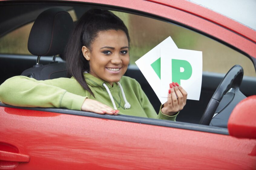 Teenage girl holding up pass signs in her car to symbolise she passed her driving test