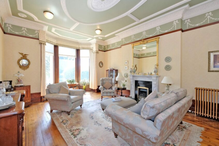 Bright lounge with ornate cornice, wooden flooring and fireplace.