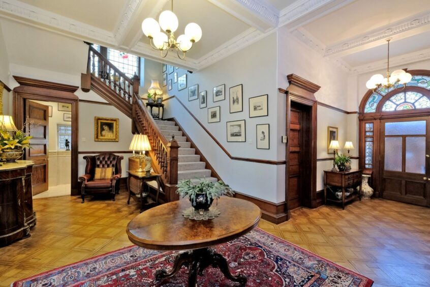 The hallway with a hardwood staircase pitch ornate plasterwork cornices, wooden doors and flooring.