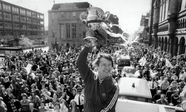 Aberdeen FC manager Alex Ferguson holds the Premier Division trophy aloft during an open-top bus parade at the Castlegate in 1980.