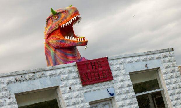The dinosaur head appears to burst through the roof of the shop.