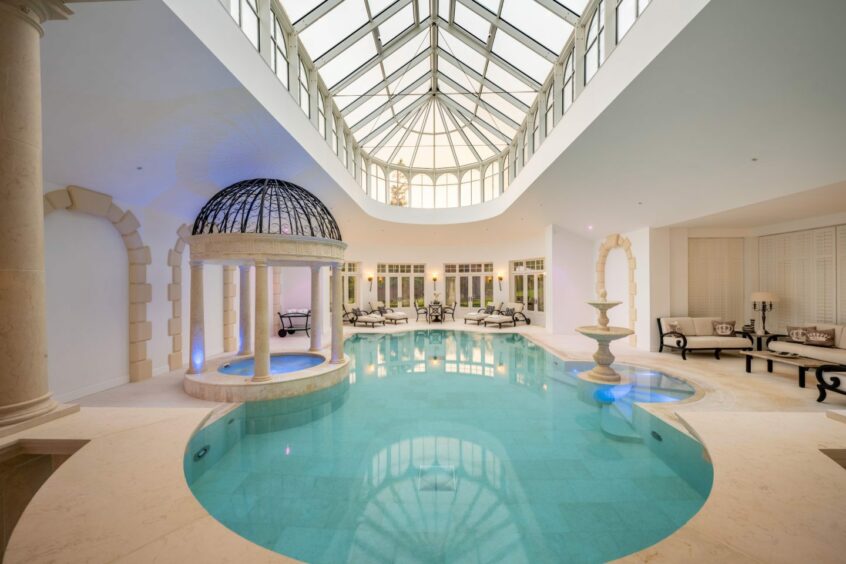 Dalhebity House's pool, underneath a glass roof, with fountain and hot tub, seating and marble flooring.