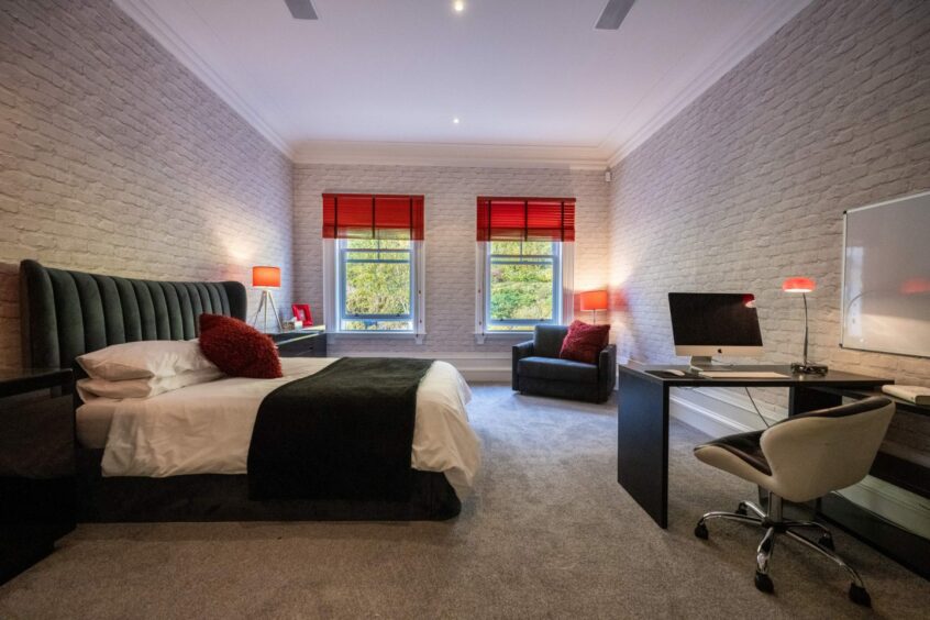 Another of the bedrooms, this one decorated with brick wallpaper, and a desk with two large windows