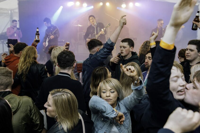 A crowd dancing in front of a stage with a band at Keith Friendly Festival.