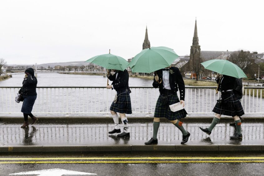 Three men wearing kilts with green umbrellas walking in the rain. World Photography Day