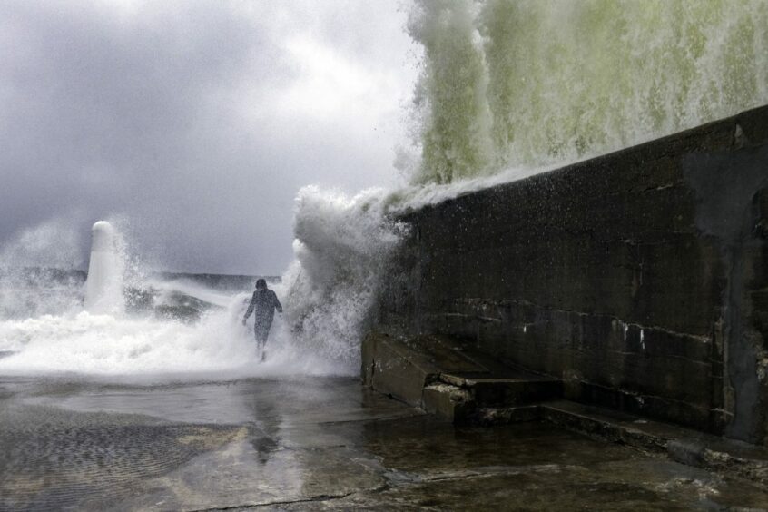 A person running towards the sea during a storm as a wave crashes against a sea wall. World Photography Day