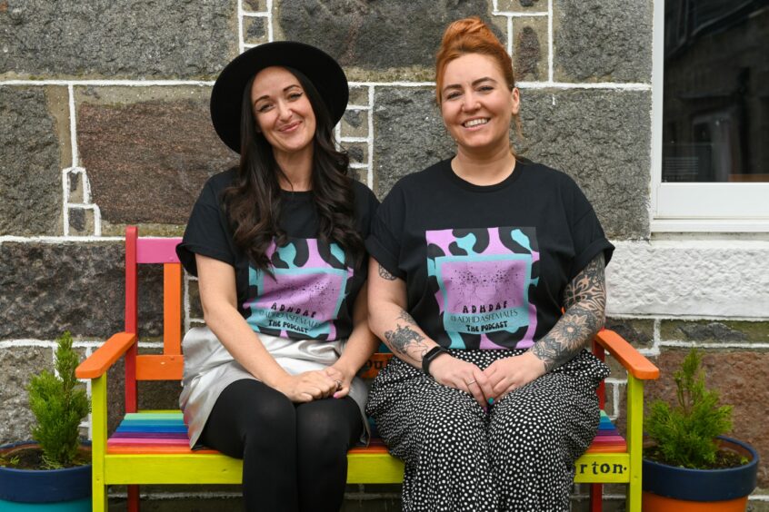 Laura Mears-Reynolds and Dawn Farner sitting on a rainbow bench outside Fittie cottage