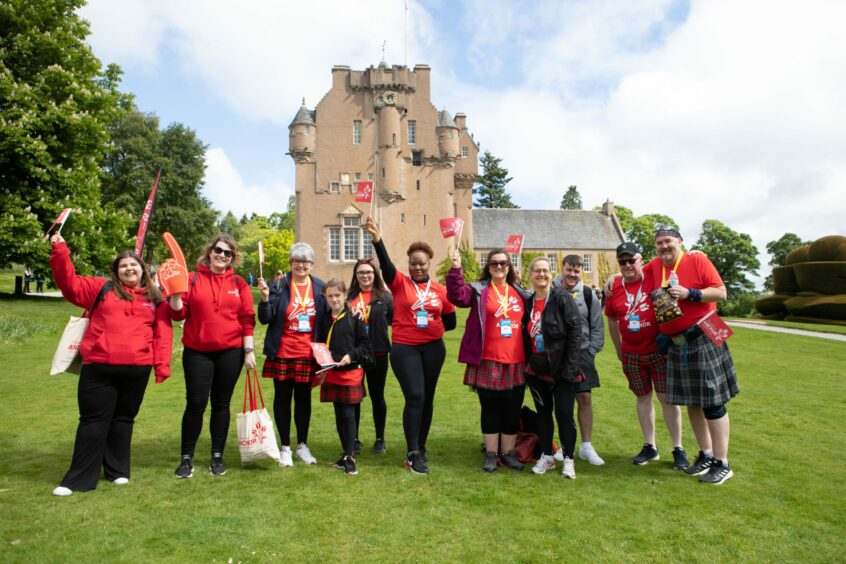 A group of walkers wearing kilts and red Friends of Anchor t-shirts in front of Crathes Castle 