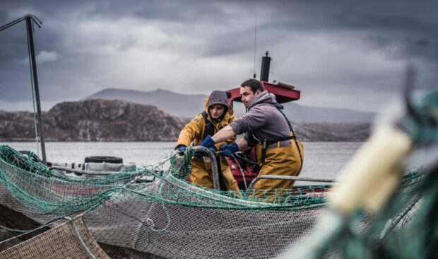 Two Loch Duart salmon farmers haul in fish against stormy skies.