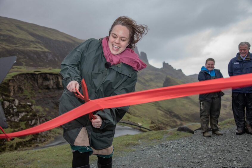 A woman cutting a red ribbon with a large pair of scissors