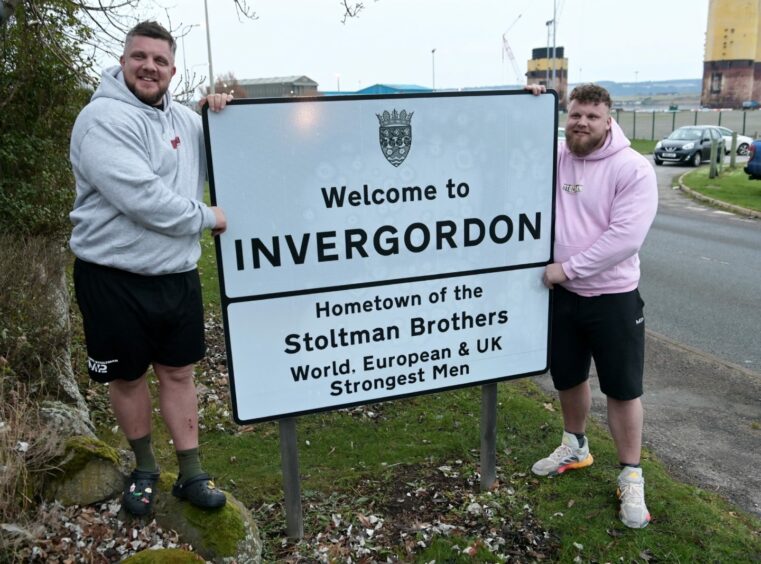 Luke and Tom Stoltman pose with the Invergordon welcome sign.