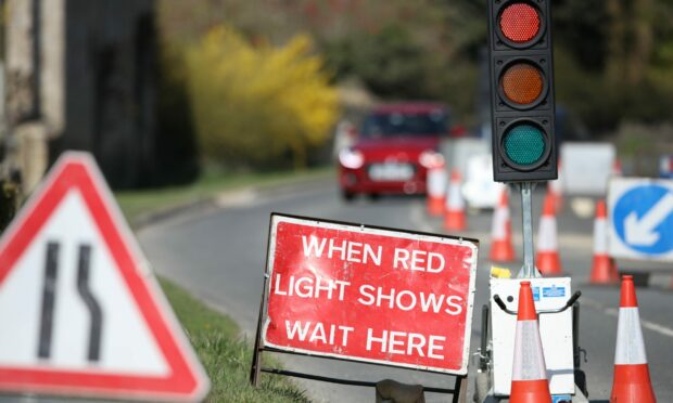 Temporary traffic lights and cones along with a sign reading "When red light shows wait here"