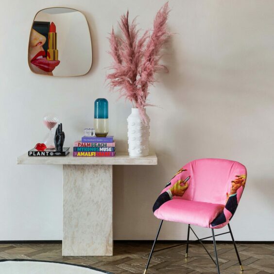 A statement pink chair with a bright print on it next to a table with unique decorations on it.
