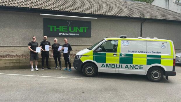 Four men standing next to an ambulance holding a certificate,