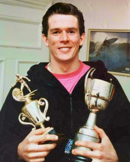 Iain Masson holding two surfing trophies