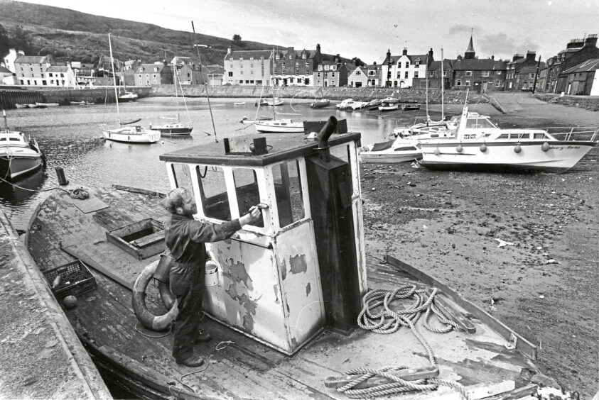 Offshore worker Ron Smith paints the wheelhouse of a friend's boat in Stonehaven harbour in 1984