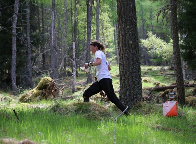 A woman running through trees while competing in the Scottish Six Days Orienteering event