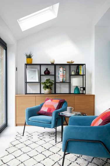 A modern, contemporary sitting room with two blue armchair and a decorated shelving unit