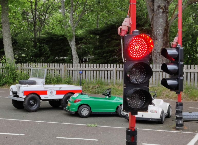 The electric cars parked next to the tracks traffic lights.