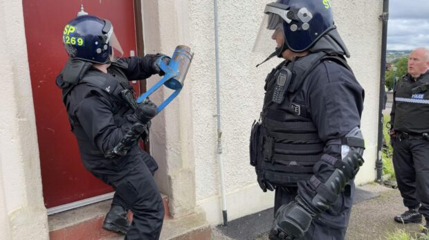 A battering ram is used by police officers to enter a home on Oscar Road in Torry.