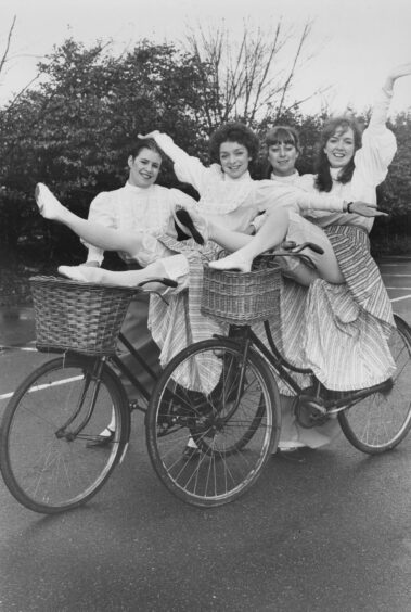 Four young Inverness women posing on old-fashioned bikes with baskets