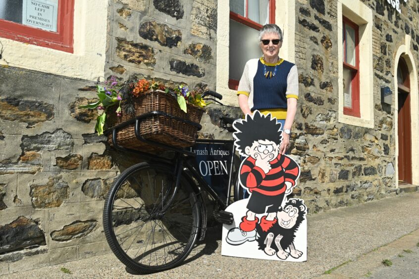Alison Milne standing outside Lynash Antiques with a cardboard cutout of Dennis the Menace