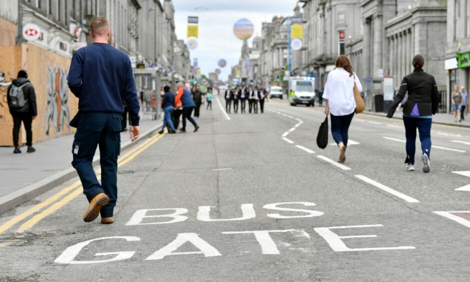 Pedestrians walk across 'Bus Gate' road marking.