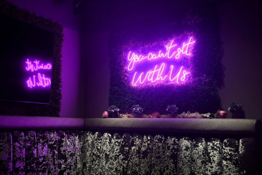 A purple neon sign reading "You can't sit with us", a quote from the movie 'Mean Girls'