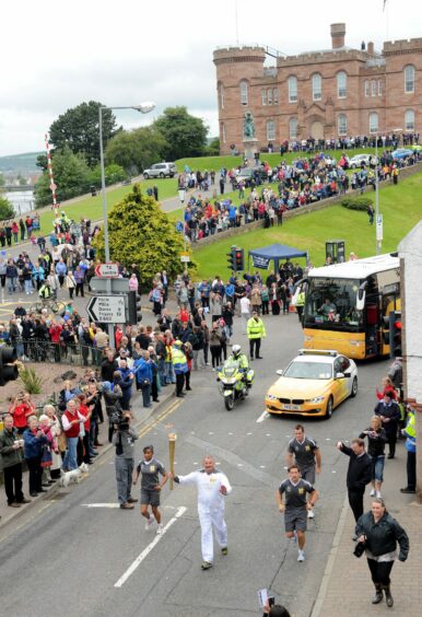 Robbie Young carrying the Olympic torch in Inverness being cheered out by by-standers.