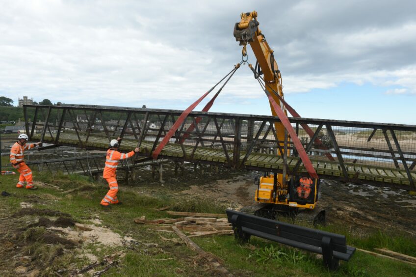 A section of the Lossiemouth bridge being moved to land by workers and a crane