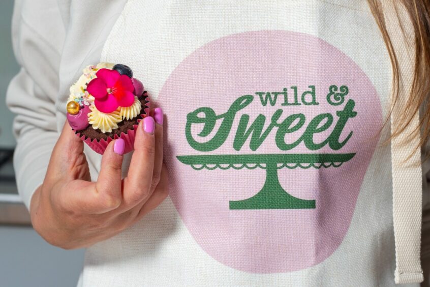 Jemma Mathieson holding a cupcake next to her 'Wild & Sweet" logo jumper.