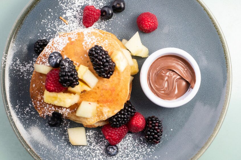 Pancakes with an assortment of berries and a small bowl of Nutella spread.