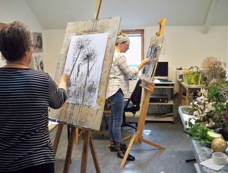 A woman paints a still life of plants on an easel.