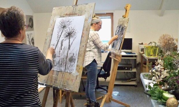 A woman paints a still life of plants on an easel.