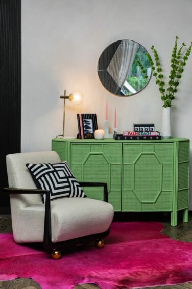 A bright, contemporary sitting area with a unique armchair, pink rug and green dresser.