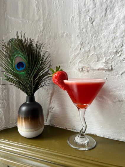 A red cocktail in a unique cocktail glass with a strawberry garnish
