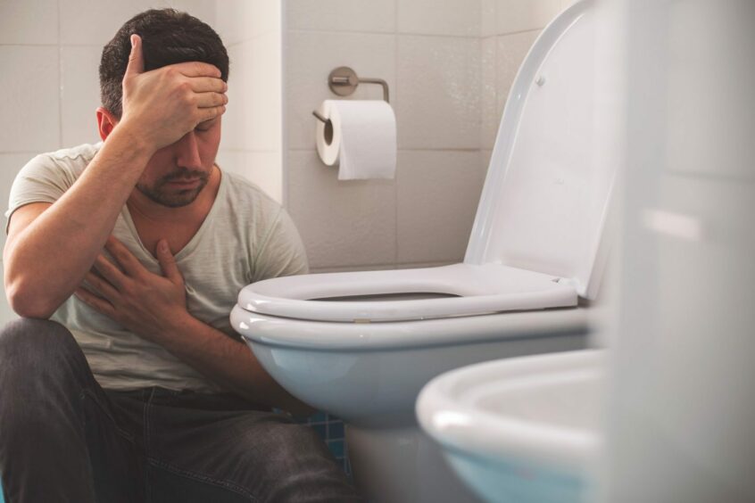 Nauseous man with headache crouching next to toilet getting ready to vomit 