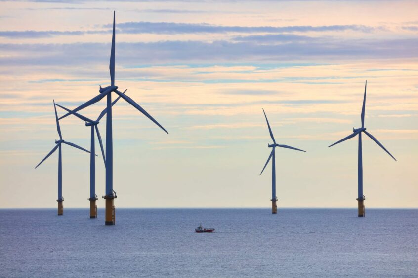 A small fishing boat dwarfed by huge wind turbines in the North Sea.