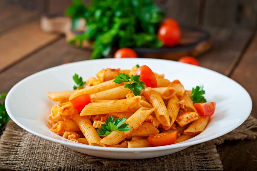 Penne pasta in tomato sauce with chicken, tomatoes decorated with parsley.