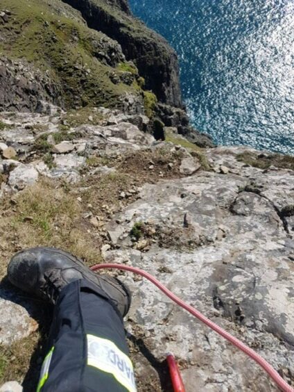 A Coastguard technician looks down a very steep slope into the sea.