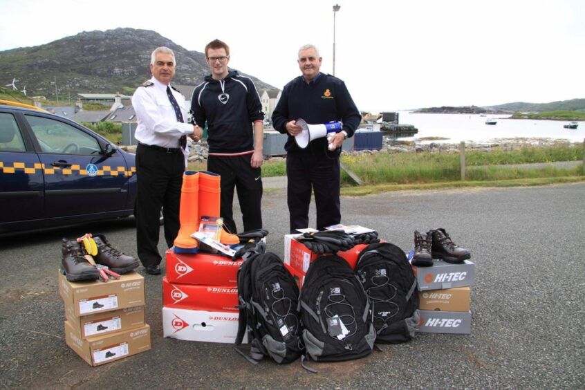 Three men stand in front of piles of new Coastguard kit.