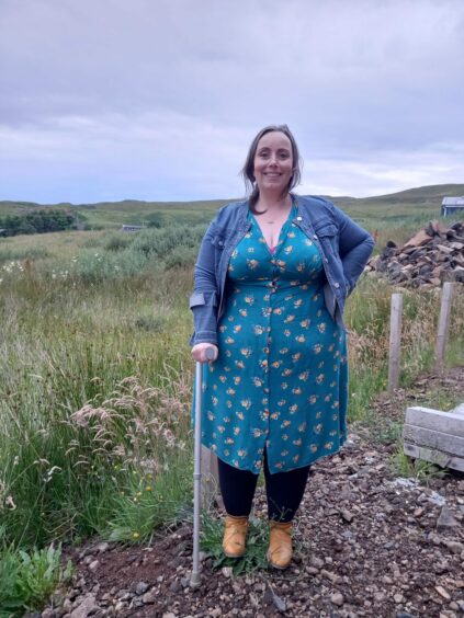 Lorna Taggart standing on path next to long grass, holding onto crutch she uses to walk