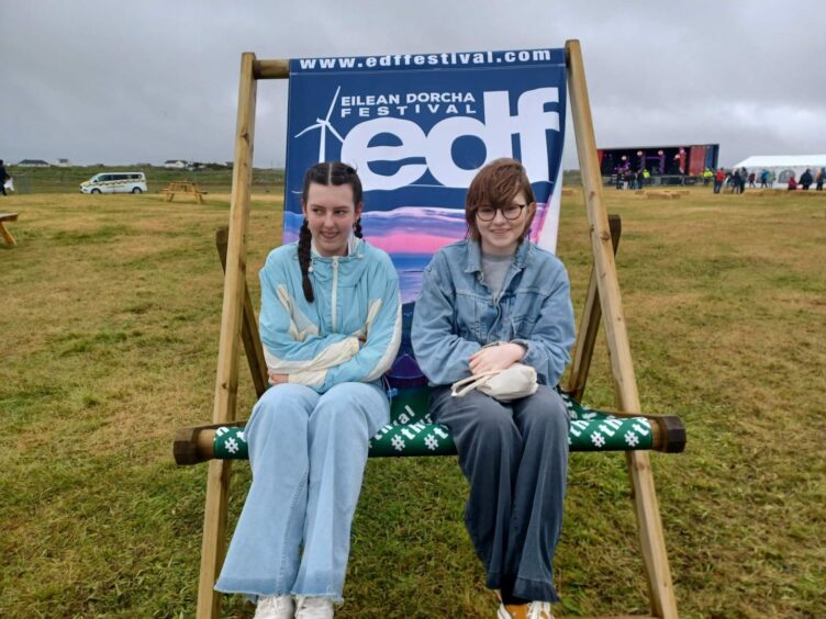Two girls sit on an oversized deck chair with EDF branding.