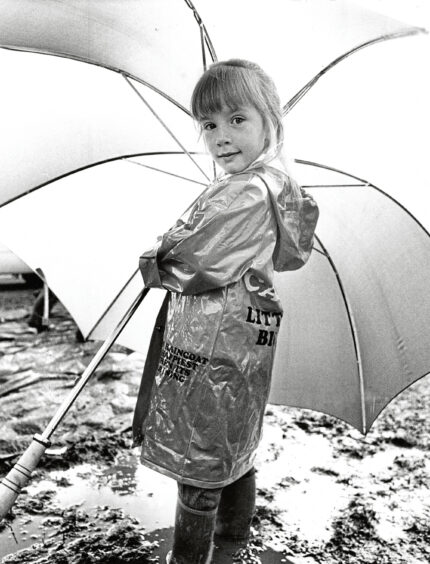 A young girl in a raincoat holding a large umbrella, ready for the echt show
