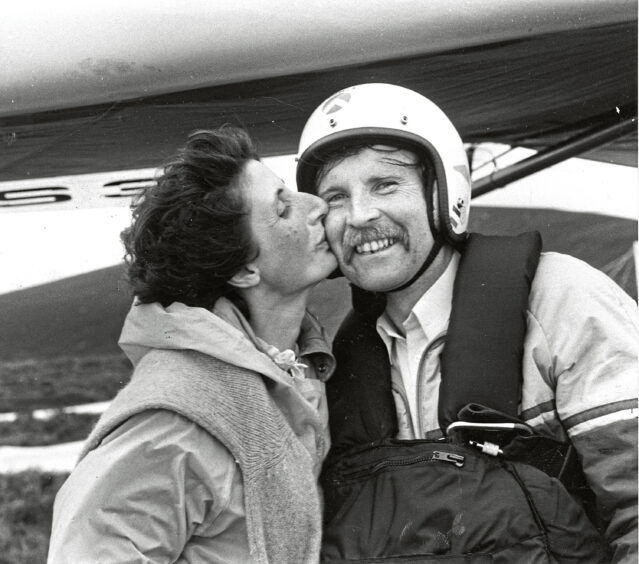 A man receiving a kiss from his wife before hang gliding