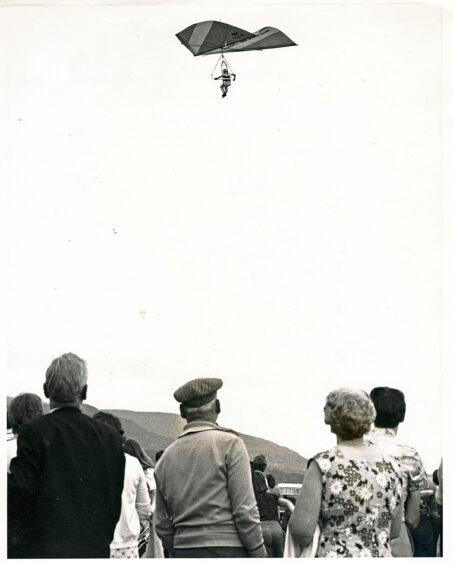A crowd of people watching a man hand gliding
