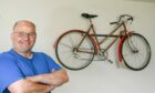 Clive Hampshire smiling with restored pushbike on the wall at their auction house in Oyne